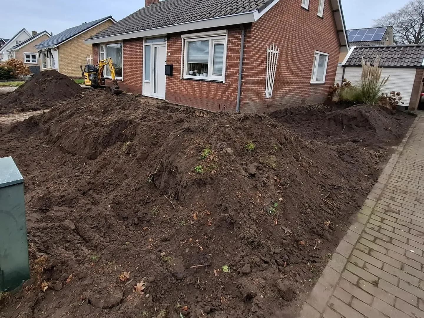 Afgegraven grond in hopen in de voortuin in Harkema, met de minigraver bij de voordeur van de vrijstaande woning