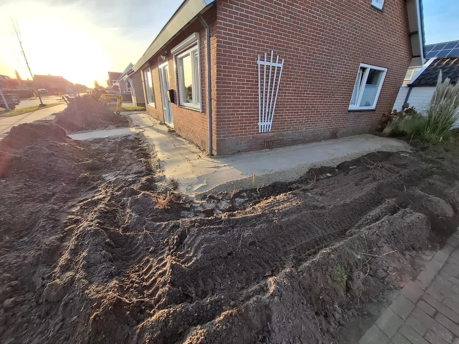 Omgewoelde grond met bandensporen en een vlak gemaakte strook langs de gevel van een woning in Harkema, bij laagstaande zon