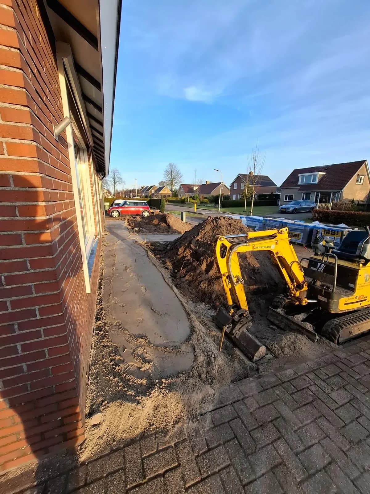 Minigraver aan het werk in de voortuin in Harkema, naast een vlak gemaakte strook zand langs de gevel voor het nieuwe pad