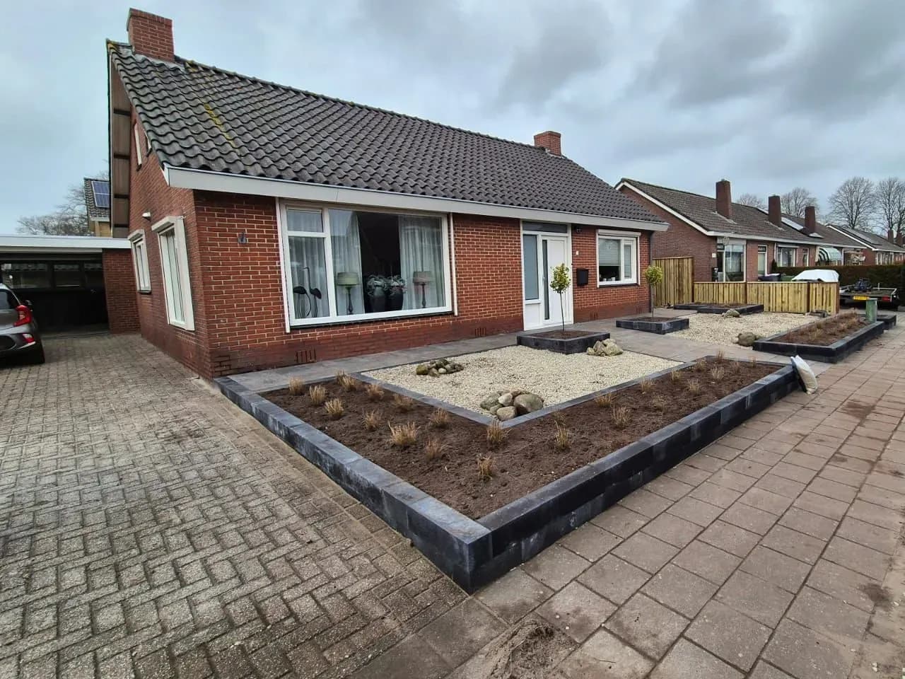 Onderhoudsarme voortuin met grind en een L-vormige verhoogde bak van stapelblokken met jonge siergrassen, bij een vrijstaande woning in Harkema