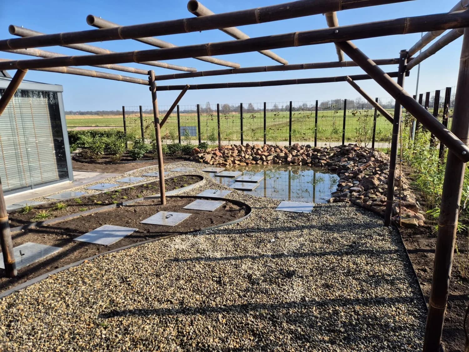 Vijver met staptegels en grind, gezien vanonder de bamboe pergola in een nieuwbouwtuin in Gorredijk