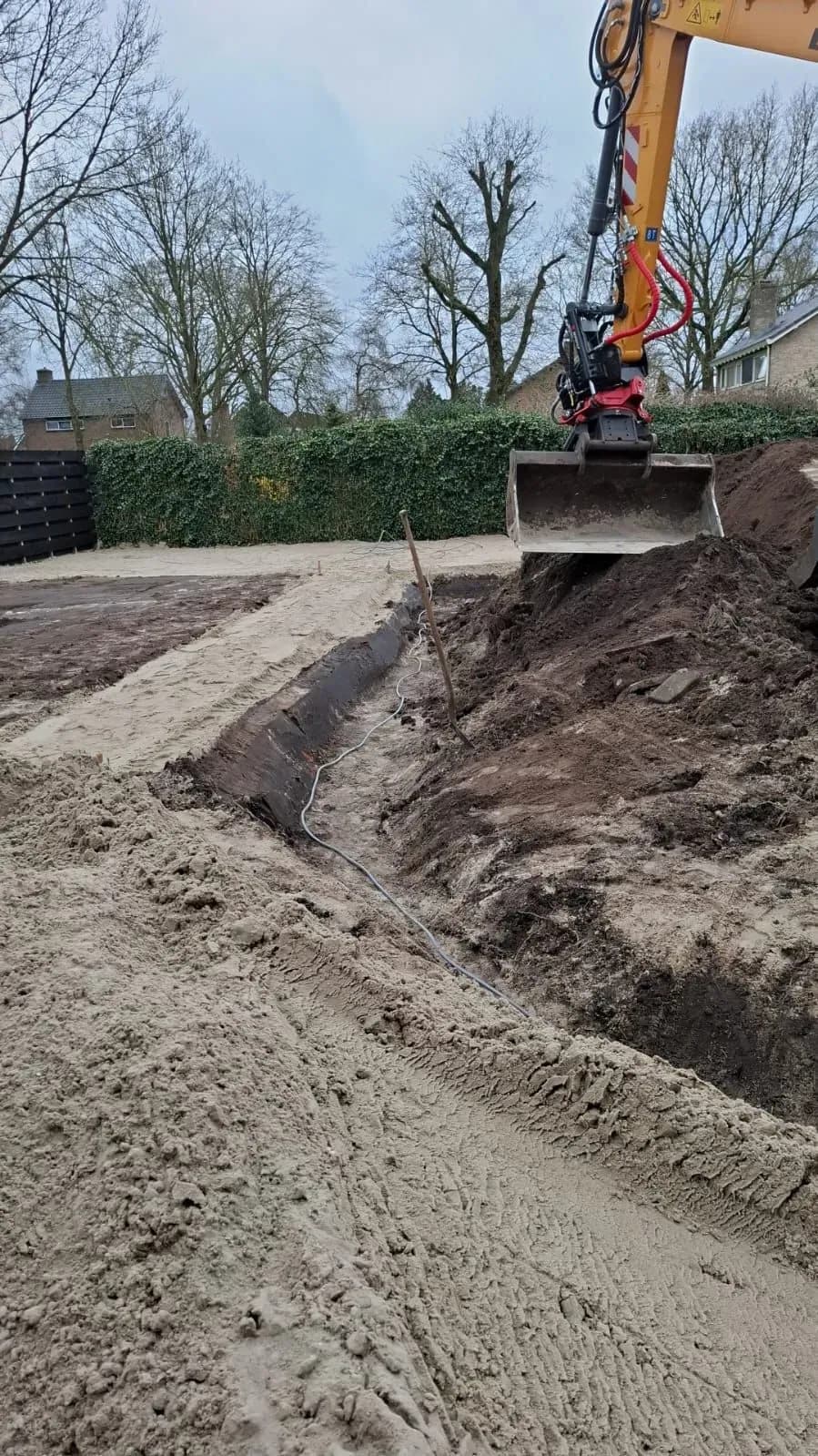 Graafmachine aan het grondwerk in de kale nieuwbouwtuin in Lippenhuizen, voor de aanleg van de familietuin