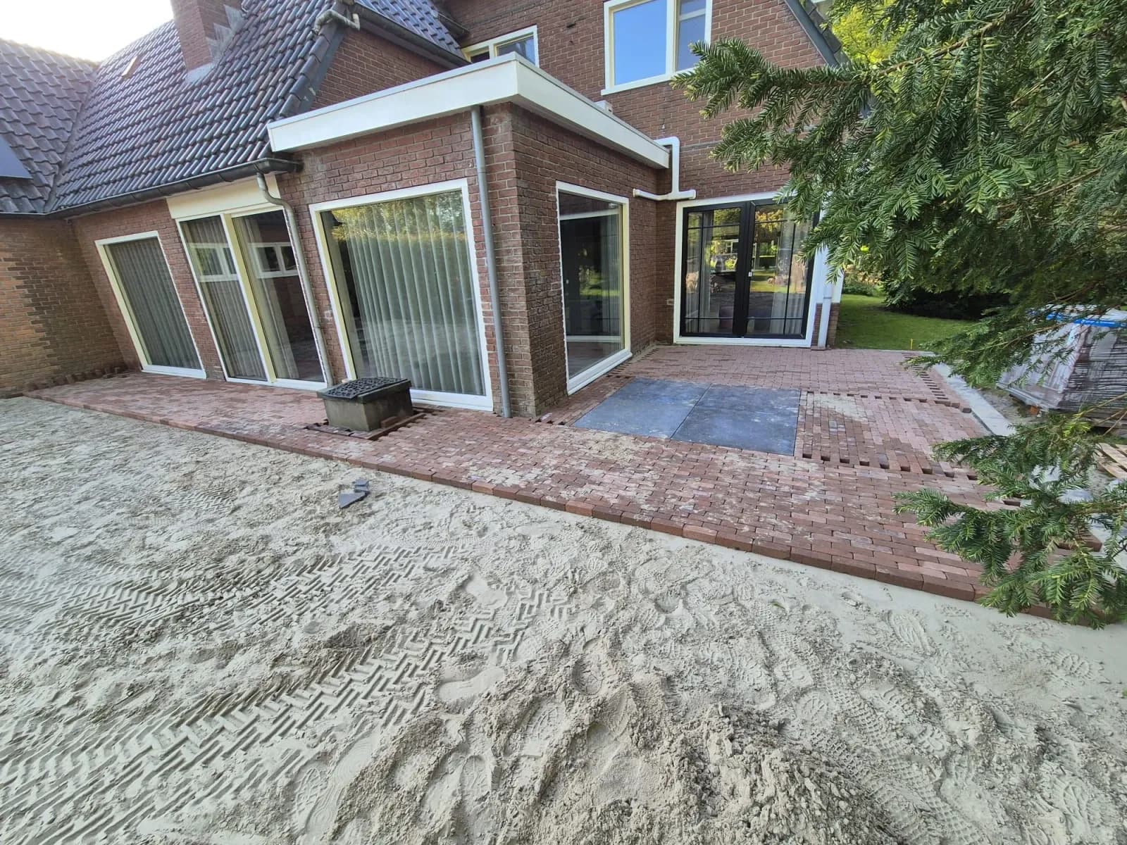 Rustiek terras in aanleg met oud-Hollandse tegels en gebakken klinkers op het zandbed langs de achtergevel van een woning in Oldeberkoop