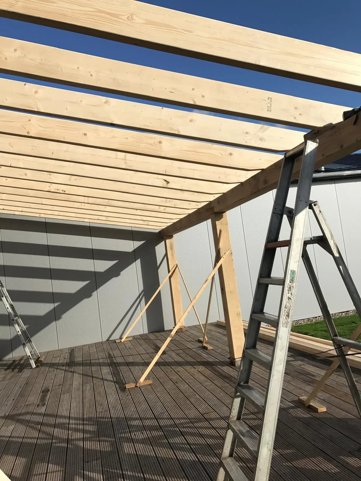 Nieuwe dakbalken tegen een blauwe lucht, gedragen door staanders met tijdelijke schoren, met twee trapladders op de vlonder