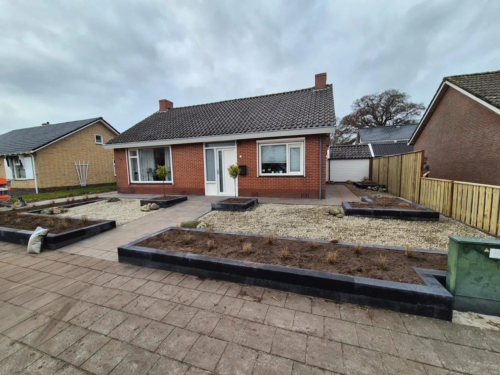 Strakke, onderhoudsarme voortuin met grind en verhoogde bakken langs de stoep, met een tegelpad naar de voordeur van een vrijstaande woning in Harkema