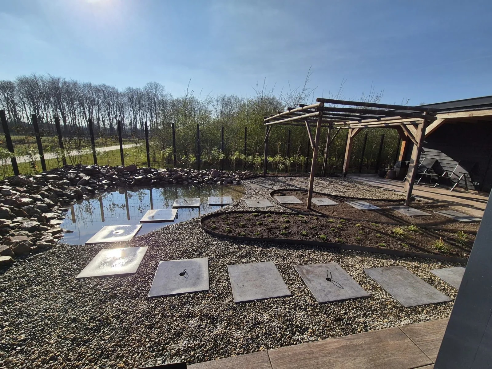 Nieuwbouwtuin in Gorredijk, Friesland, met een vijver, staptegels door het water en een pergola van bamboe
