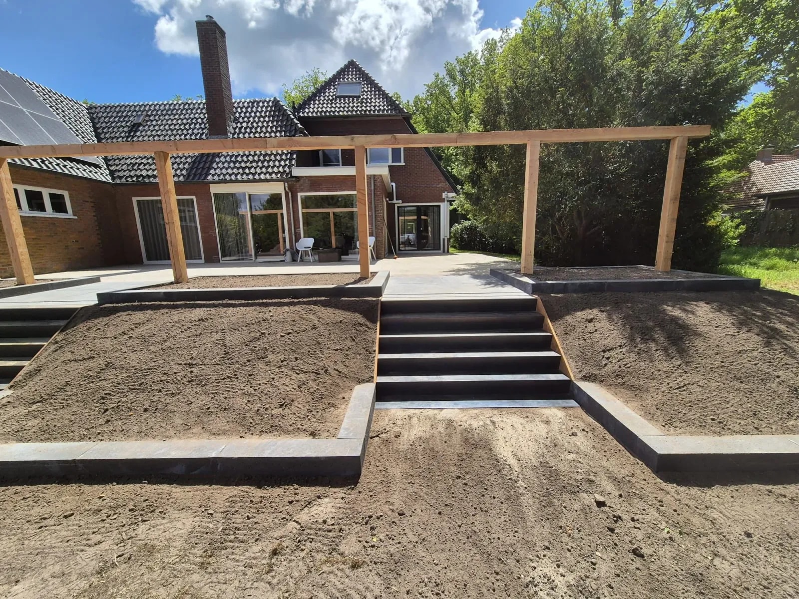 Verhoogd terras met trap en een pergola van douglas, gezien vanuit de lagere tuin in Oldeberkoop, met nieuwe borders in aanleg