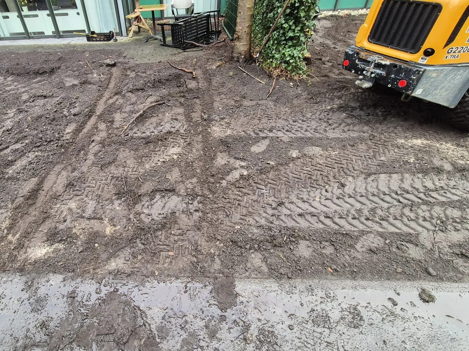 Losgemaakte grond met bandensporen voor de glazen gevel van zorglocatie Voltawerk in Gorredijk, aan het begin van de aanleg van de belevingstuin
