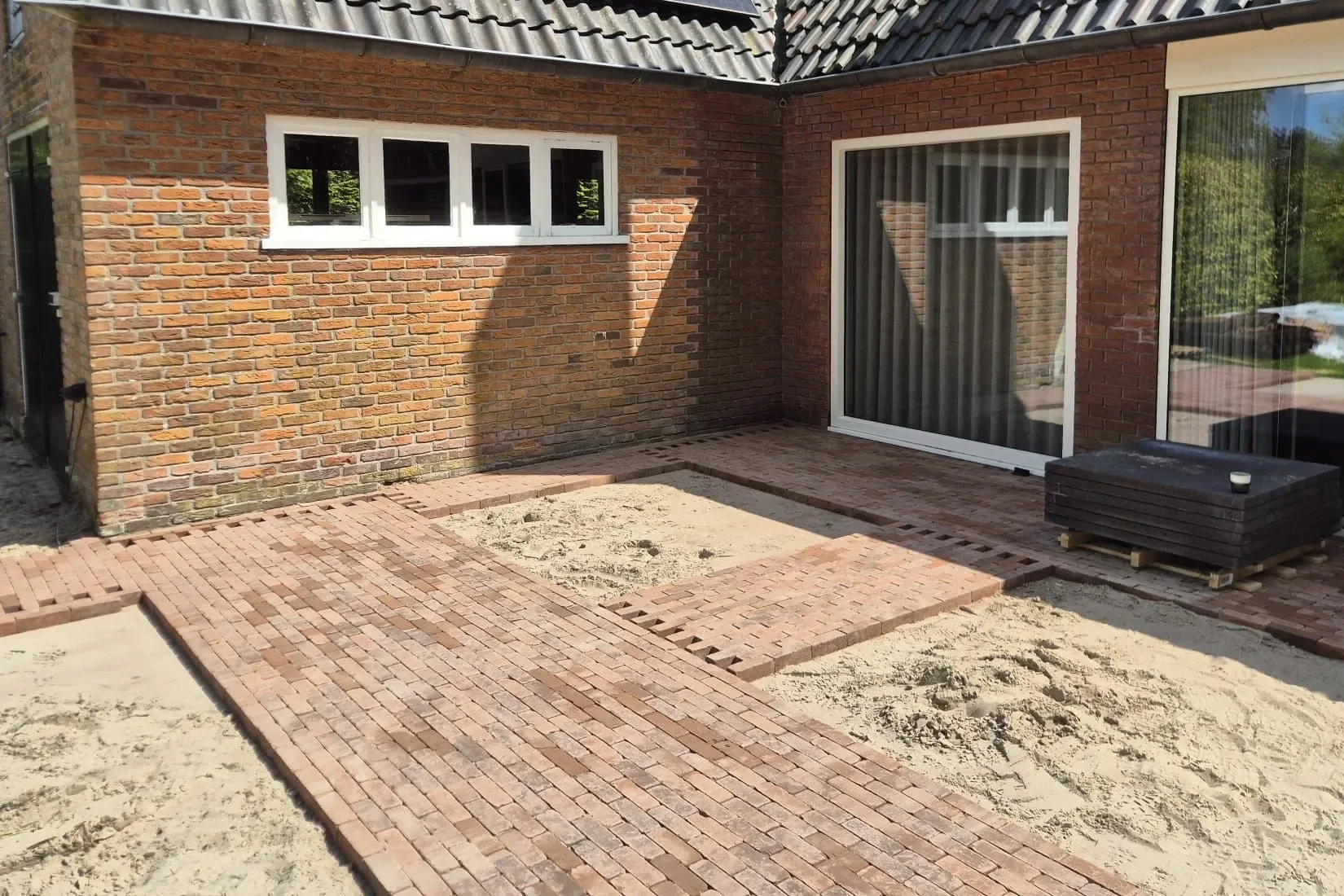 Terras in Oldeberkoop tijdens het bestraten: banen van gebakken klinkers langs de gevel, met vakken van zand ertussen