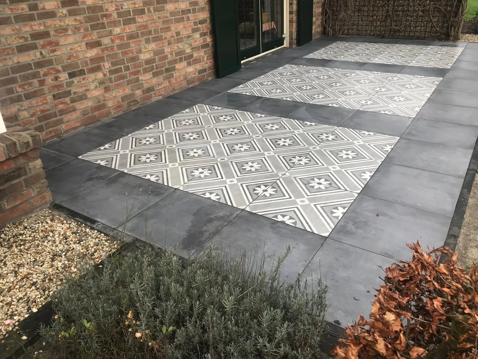 Terras bij de gevel met vlakken van grijs-witte patroontegels in een kader van antraciet tegels, met lavendel ervoor