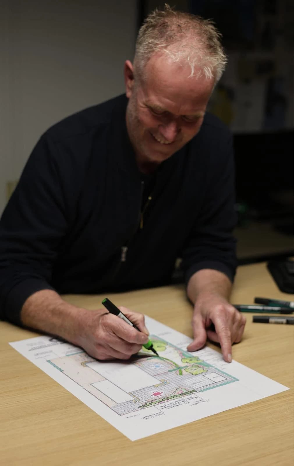 Feitze Dijkstra kleurt aan tafel een tuinontwerp in met een groene stift
