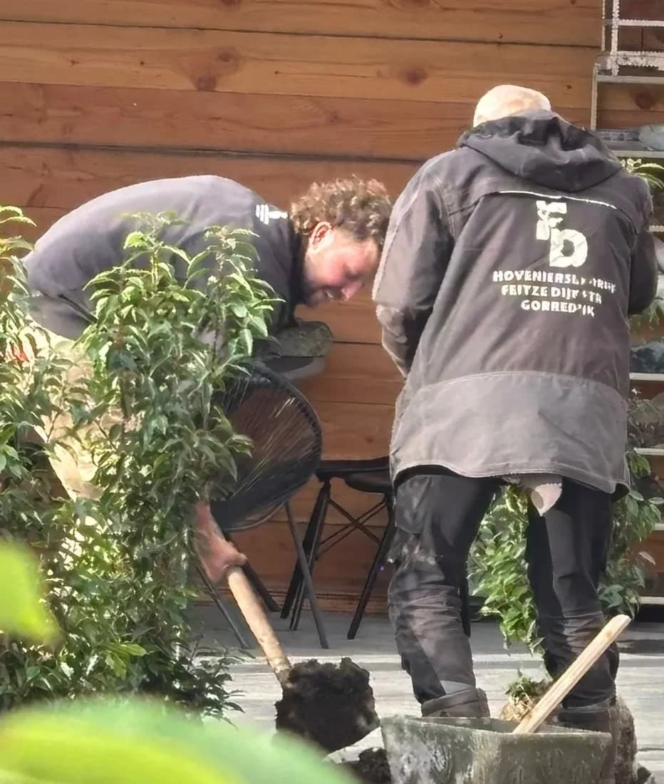 Twee hoveniers, een in een jas van Hoveniersbedrijf Feitze Dijkstra, planten heesters onder een houten overkapping in De Vrieswijck in Gorredijk