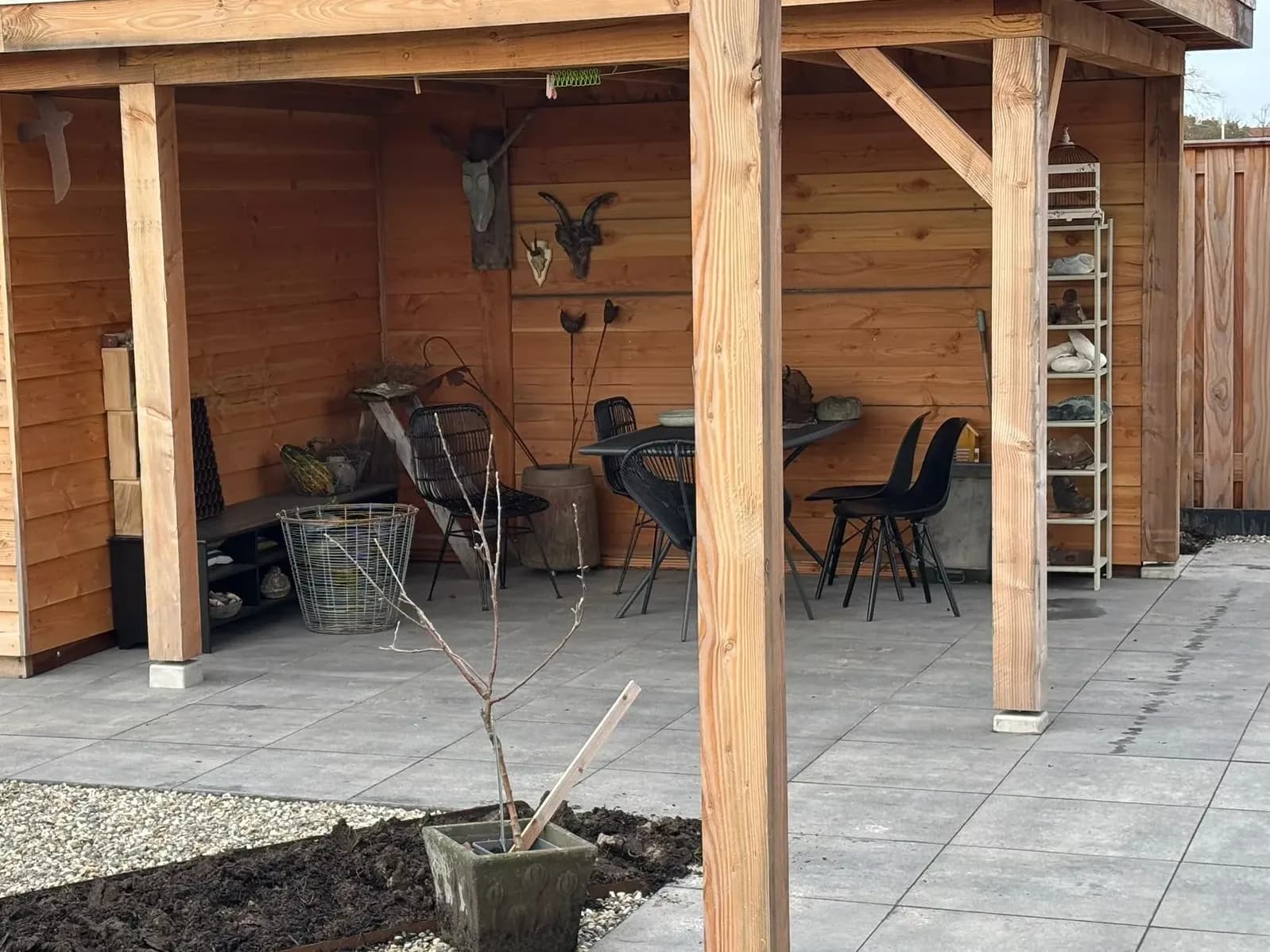 Houten overkapping met een berging en een zithoek op een terras van grote tegels, met grind en een border met een rand van cortenstaal ervoor, in De Vrieswijck in Gorredijk