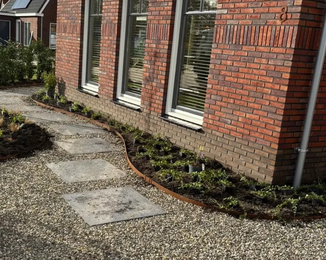 Pad van grote betontegels in grind langs een nieuwbouwwoning in De Vrieswijck in Gorredijk, met een gebogen cortenstalen rand en jonge beplanting