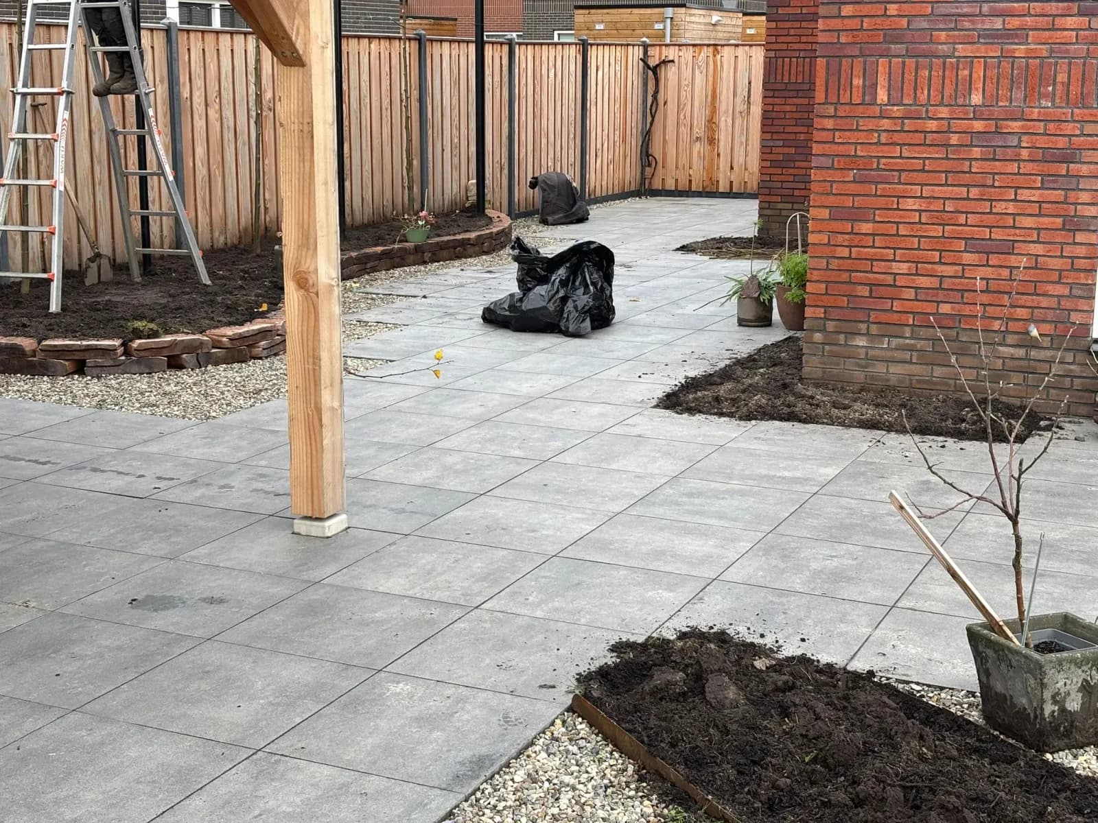 Strak betegeld terras met grind langs de rand, een staander van de houten pergola en een nieuwe border met een muurtje van gestapelde stenen langs de schutting, bij een vrijstaande woning in De Vrieswijck in Gorredijk